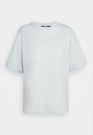 Světle modré bavlněné tričko s krátkými rukávy, kulatým výstřihem, volným střihem a jemně vyraženým logem na hrudi. Hladká textura.