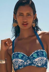 Zils ziedu push-up bikini tops ar veidotiem krūšturiem, regulējamām siksnām un tropisku rakstu, kas ietver lapas un ananāsus. Sudraba rokassprādze un auskari.