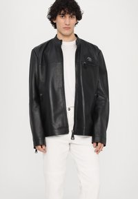 Veste en cuir noir avec col montant, fermeture zippée à l'avant et poche poitrine zippée. Comprend des poches latérales et une texture lisse.