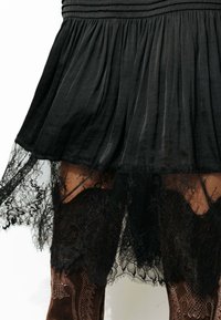 Robe noire plissée avec bordure en dentelle. La dentelle est détaillée et festonnée, superposée à une jupe intérieure plus courte. Le tissu extérieur a une texture lisse.