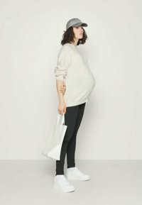 Tenue de maternité comprenant un pull de couleur claire, des leggings noirs, des baskets blanches et une casquette grise, accompagnée d'un tote bag blanc.
