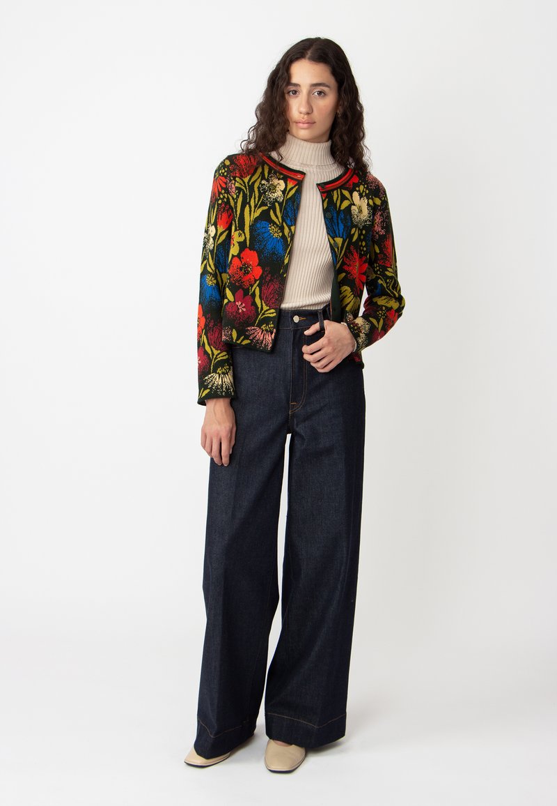 Veste courte à motif floral de plusieurs couleurs, associée à un jean en denim noir à taille haute et à pattes larges, ainsi qu'à un col roulé crème côtelé.