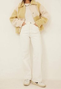 Kurtka polarowa w beżowe i kremowe paski, z zatrzaskowym zapięciem i kołnierzem, noszona z białymi spodniami o wysokim stanie i białymi trampkami.