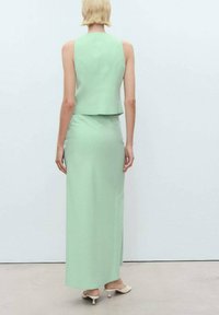 Ensemble vert menthe en deux pièces comprenant un haut sans manches et une jupe longue, en tissu lisse avec une silhouette ajustée. Chaussures à petit talon.