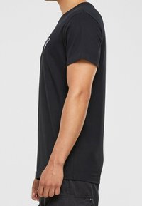 Černé bavlněné tričko s krátkými rukávy, kulatým výstřihem a rovný střih. Obsahuje minimalistické logo na hrudi.