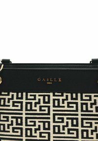 Borsa a tracolla in bianco e nero con un corpo in tessuto texturizzato e una parte superiore in pelle liscia. Presenta lettering e accessori in oro.