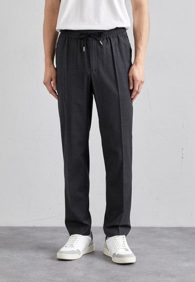 Pantaloni jogger ușori, de culoare gri închis, cu talie elastică și șnur. Purtați cu adidași albi pe o podea texturată.