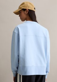 Lichtblauwe sweatshirts met een ronde hals en geribde manchetten, voorzien van een gladde textuur en een losse pasvorm. Draagt een beige baseballpet.