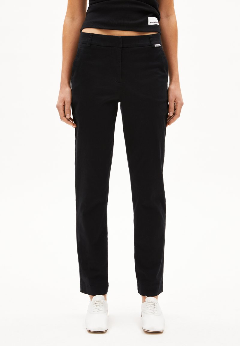 Zwarte rechte broek van katoen, met een platte voorkant, riemlussen en een subtiele merklabel op de tailleband. Gepaard met witte schoenen.