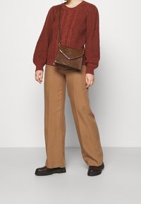 Rode gebreide trui met textuur en lange mouwen, gecombineerd met beige wijde broek en bruine enkelbotten. Bruine crossbody tas met krokodillenpatroon.