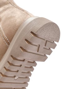 Suela de zapato de ante beige con surcos texturizados y un tacón redondeado y ligeramente elevado. La suela exterior presenta un patrón de tracción resistente y multidireccional.
