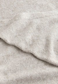 Lys grå, tekstureret stof med et blødt, strikket udseende, der har subtile farvevariationer og en let foldet kant.