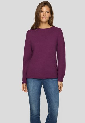 Lila gerippter Pullover mit rundem Halsausschnitt und langen Ärmeln, kombiniert mit blauen Jeans. Die Textur ist strukturiert und körpernah.