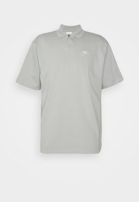 Light grey polo shirt made of cotton with a three-button collar and a small white Nike logo on the chest. Short sleeves, relaxed fit.