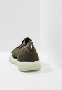 Scarpa atletica verde scuro con tomaia testurizzata, dettagli neri, suola spessa bianca e verde menta, e logo sul tallone.