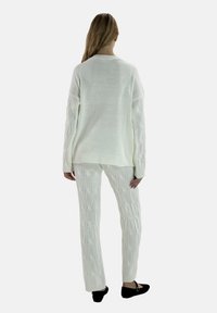 Hvid strikket sweater med dropped skuldre og ribbet kant, parret med matchende kabelstrikkede bukser. Tekstureret stof og afslappet pasform hele vejen igennem.
