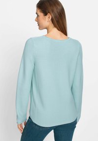 Hellblau strukturierter Pullover mit langen Ärmeln und rundem Ausschnitt, der einen leicht gebogenen Saum und seitliche Schlitze für eine verbesserte Passform aufweist.