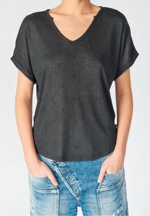 Sort kortærmet V-hals top med små perleudsmykninger båret med lyseblå denimbukser med lappelommer.