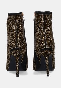 Botines negros con tacón de aguja, cubiertos de tachuelas doradas, con una cremallera lateral a lo largo de la costura para fácil colocación.