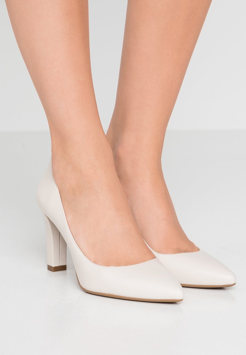 Bottines à talons hauts en cuir verni beige avec un bout pointu et un talon carré. Texture lisse avec un design minimaliste.