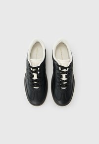Een paar zwarte leren sneakers met witte tongen en zwarte veters, vanuit bovenaf bekeken op een effen witte achtergrond.