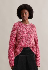 Rot-weißer gestrickter Pullover mit lockerer Passform, rundem Ausschnitt und überschnittenen Schultern. Getragen über einem schwarzen Cordrock.