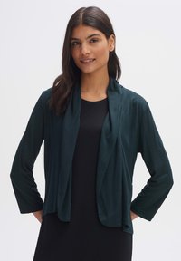 Dark green open-front cardigan made of soft fabric. Features a draped neckline and three-quarter sleeves, displayed over a black top.