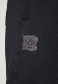 Černá látka s šedou vyšívanou nášivkou zobrazující býčí hlavu, našitou blízko vertikálního švu.