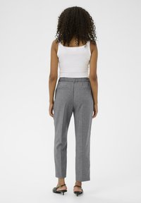 Pantalons gris ajustés en tissu texturé, coupe slim, avec une ceinture élastique, portés avec un débardeur blanc et des sandales à talons noires.