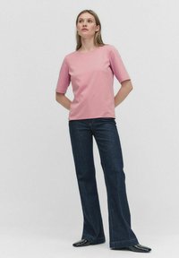 Rosa kortärmad skjorta med rund halsringning, parat med mörkblå utsvängda jeans. Toppen har en mjuk textur; jeansen har diskret sömnad.