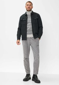 Dunkelgraue Wolljacke mit zwei vorderen Taschen, gemusterter Strickpullover in Weiß und Blau, hellgraue Cordhosen und schwarze Schnürstiefel.