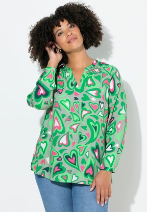 Groene blouse met korte mouwen met een hartpatroon in roze, wit en groen. V-hals ontwerp en lichtgewicht, gladde stof.