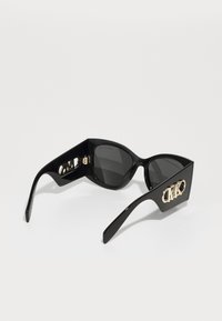 Ochelari de soare din plastic negru cu lentile întunecate, cadru unghiular și logo MK auriu pe lateral. Design elegant cu finisaj lucios.