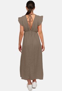 Robe longue taupe en tissu texturé, avec des manches à volants et un dos nu maintenu par des liens. Portée avec des baskets blanches.
