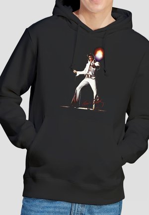 Black hoodie featuring a graphic of a performer in a white jumpsuit striking a dynamic pose with a microphone and flare effect.