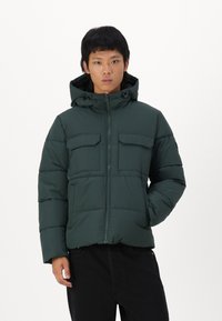Dark green puffer jacket with a hood, featuring two chest pockets, a zip front, and quilted detailing. Made from a smooth, durable material.