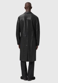 Cappotto in pelle nera con taglio dritto, cuciture visibili e texture liscia. Presenta un colletto classico e maniche lunghe.