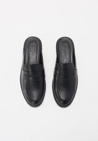 Black leather slip-on shoes featuring a rounded toe, smooth texture, and a band across the upper with subtle detailing. Brand name embossed inside.