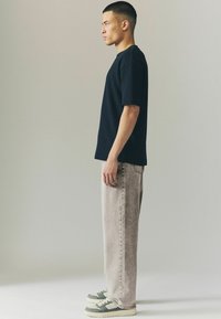 Zwarte katoenen t-shirt met een relaxte pasvorm, gecombineerd met lichtgrijze denim jeans. Sneakers hebben groene accenten en een gestructureerde zool.