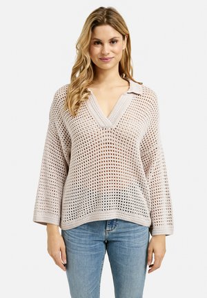 Helle beige gehäkelte Sweater mit V-Ausschnitt, kurzem Kragen und weiten Ärmeln. Die offene Maschenstruktur erzeugt ein strukturiertes Muster im gesamten Kleidungsstück.