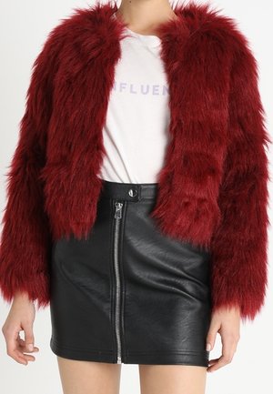 Rød imiteret pelsjakke båret over en hvid grafisk t-shirt, kombineret med en sort sort lædernederdel med høj talje og lynlåsdetalje foran.