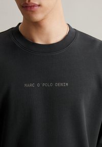 Schwarzer Sweatshirt aus weichem Stoff, mit einem gerippten Ausschnitt und dem Text "MARC O'POLO DENIM" in heller Farbe auf der Vorderseite.