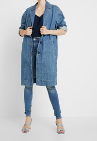 Överdimensionerad blå denimjacka med knappstängningar och uppvikta ärmar, buren över en marinblå topp och ihop med tajta jeans och ljusblå klackar.