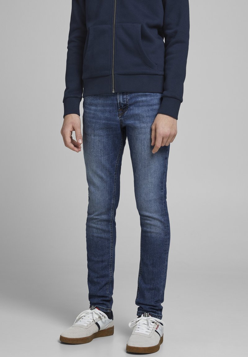Dark blue zip-up sweatshirt with front pockets, paired with slim-fit, light blue jeans and white sneakers with navy and red accents.