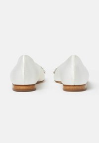 Bailarinas de satén blanco con un bajo tacón de madera, punta afilada y una textura suave, que presentan costuras sutiles y acentos decorativos en los laterales.