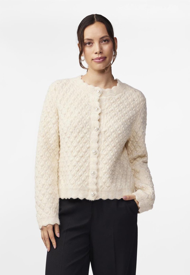 Cremfarbener strick cardigan mit einem strukturierten, diamantartigen Muster, gewelltem Ausschnitt und großen Perlenknöpfen auf der Vorderseite. Die Ärmellänge ist lang.