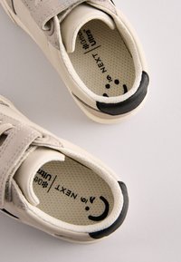 Beežid spordijalatsid tekstureeritud siseküljega, takjapael ja mustad detailid kannal. Varustatud polsterdatud sisetallaga, millel on brändi märk.