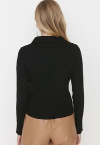 Černý žebrovaný svetr s límečkem, dlouhými rukávy a přiléhavým střihem. Nosený s světle hnědými kalhotami s vysokým pasem.