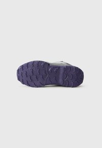 Sole di una scarpa grigia con una suola in gomma viola robusta e caratterizzata da un battistrada profondo, progettata per l'uso all'aperto o su sentieri.