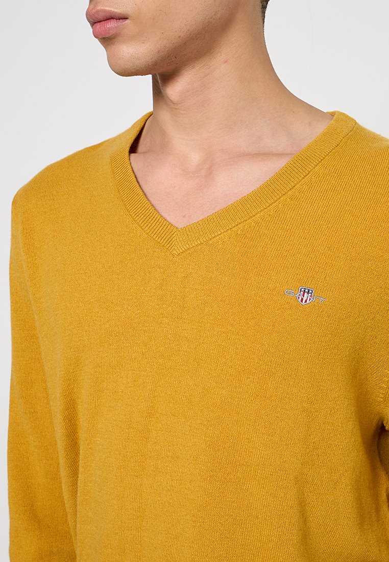 Gul v-ringad tröja i mjukt stickat material, med en liten, broderad logotyp på bröstet och en strukturerad yta.